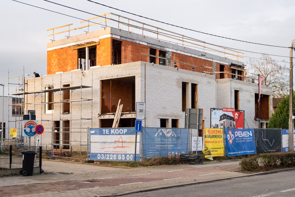 Appartementsgebouw in opbouw met witte gevelsteen, kale ruwbouw voor gevelbekleding te plaatsen en het plat dak in opbouw.