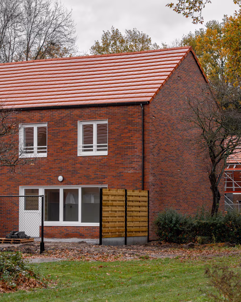Achtergevel van gerenoveerde woning met rode gevelsteen, rode dakpannen en witte ramen.