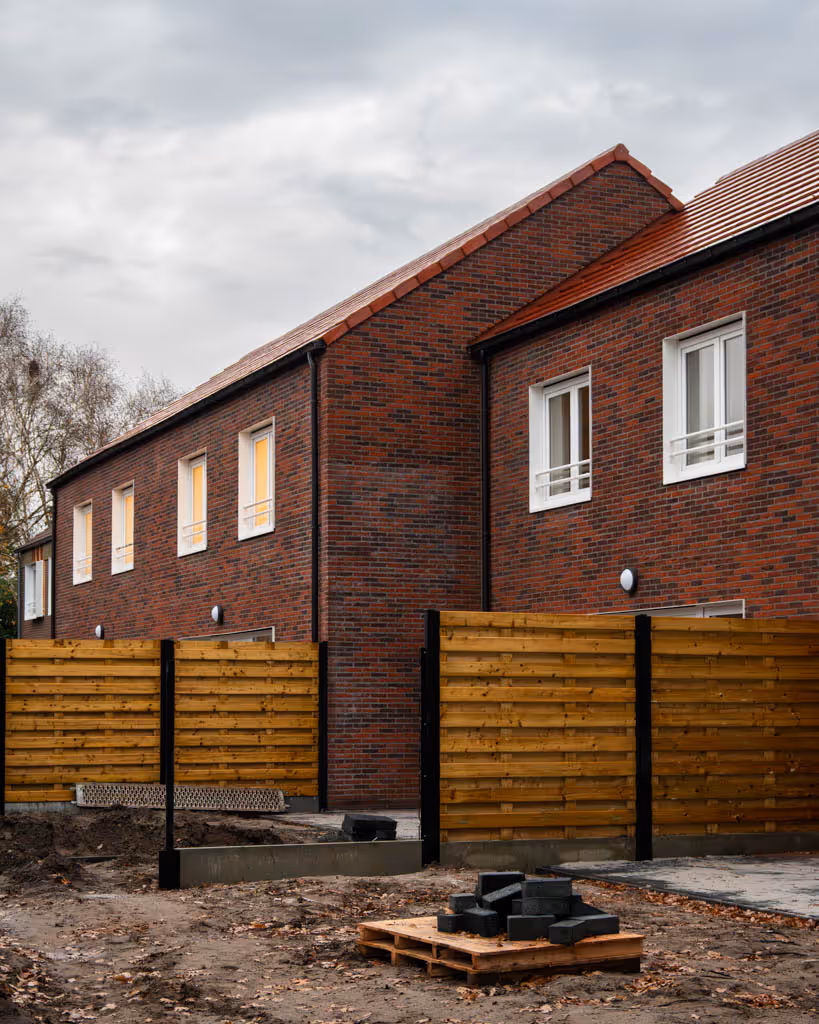 Achtergevels van gerenoveerde woningen met rode gevelsteen, rode dakpannen en witte ramen.
