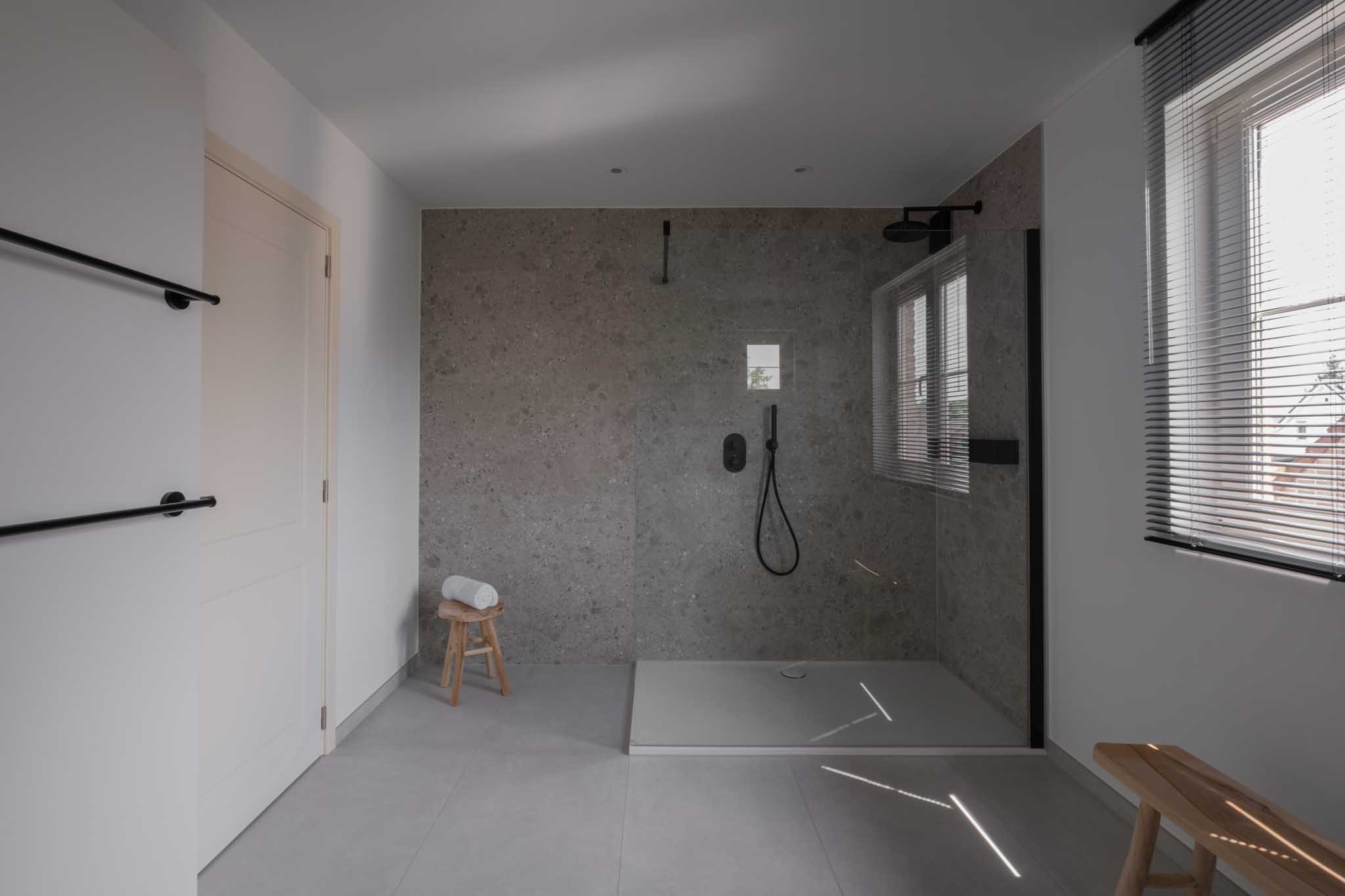 Moderne minimalistische badkamerrenovatie met grijze tegelvloer, radiator, inloopdouche en zwart kraanwerk.