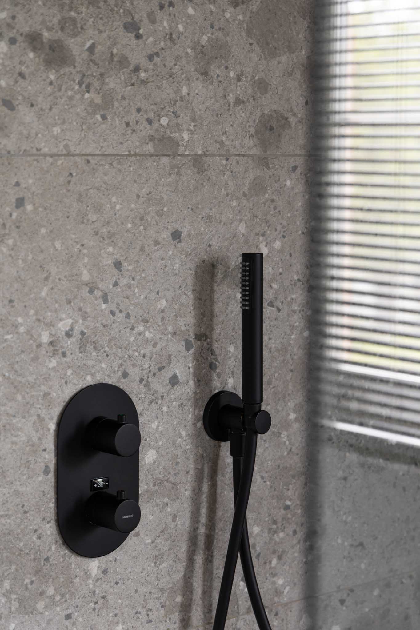 Moderne badkamer na renovatie met als detail de zwarte douchekop, en de reflectie van het raam in de douchewand.