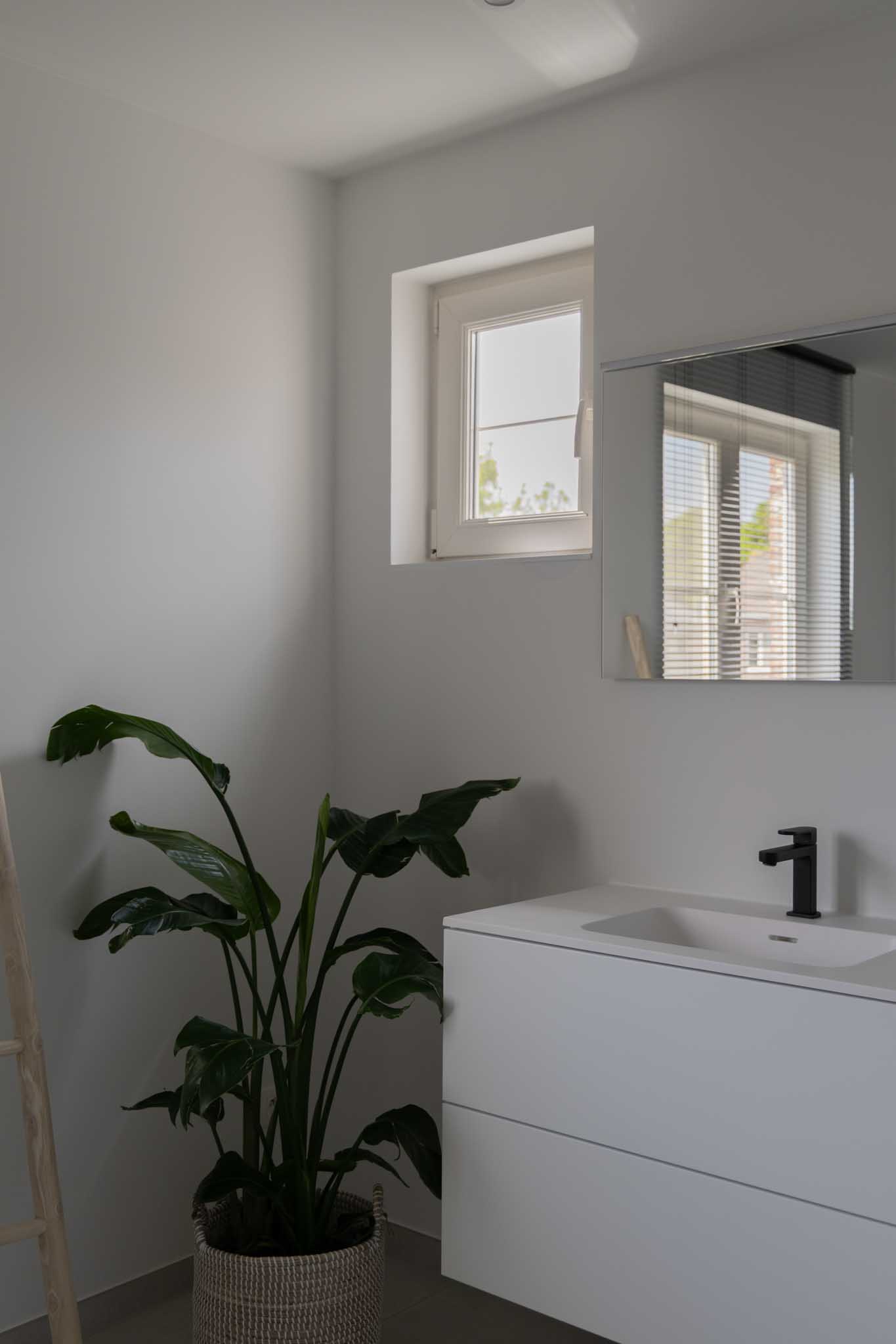 Moderne badkamer na renovatie met wit badkamermeubel, grote spiegel en extra raam.