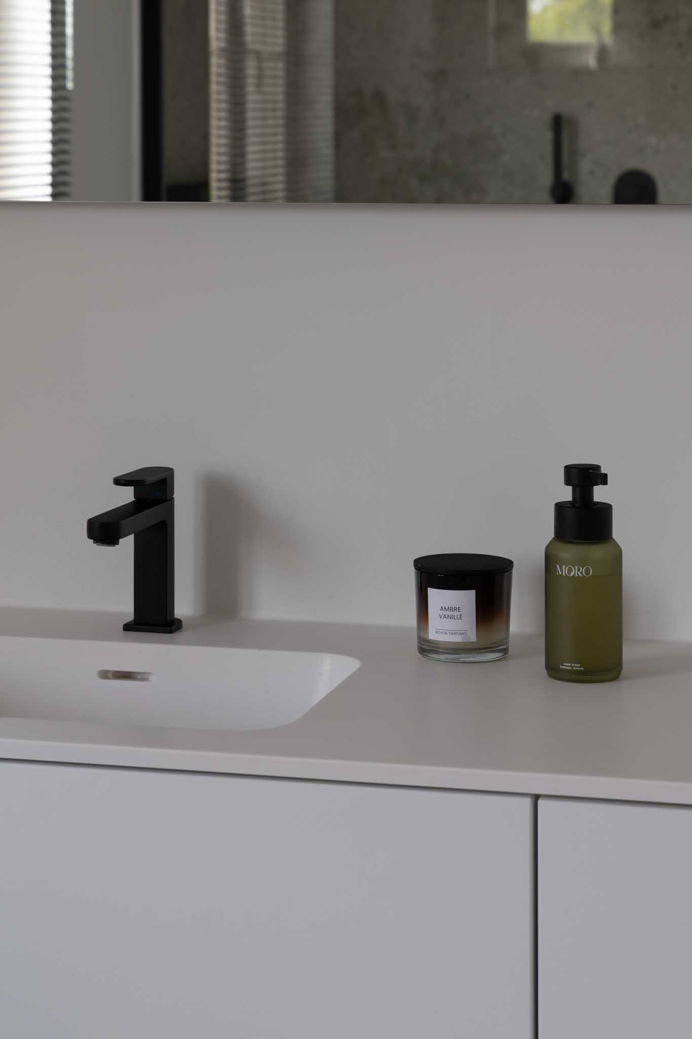 Moderne badkamer na renovatie met als detail de witte spoelbak, zwarte kraan en zeepbakjes.