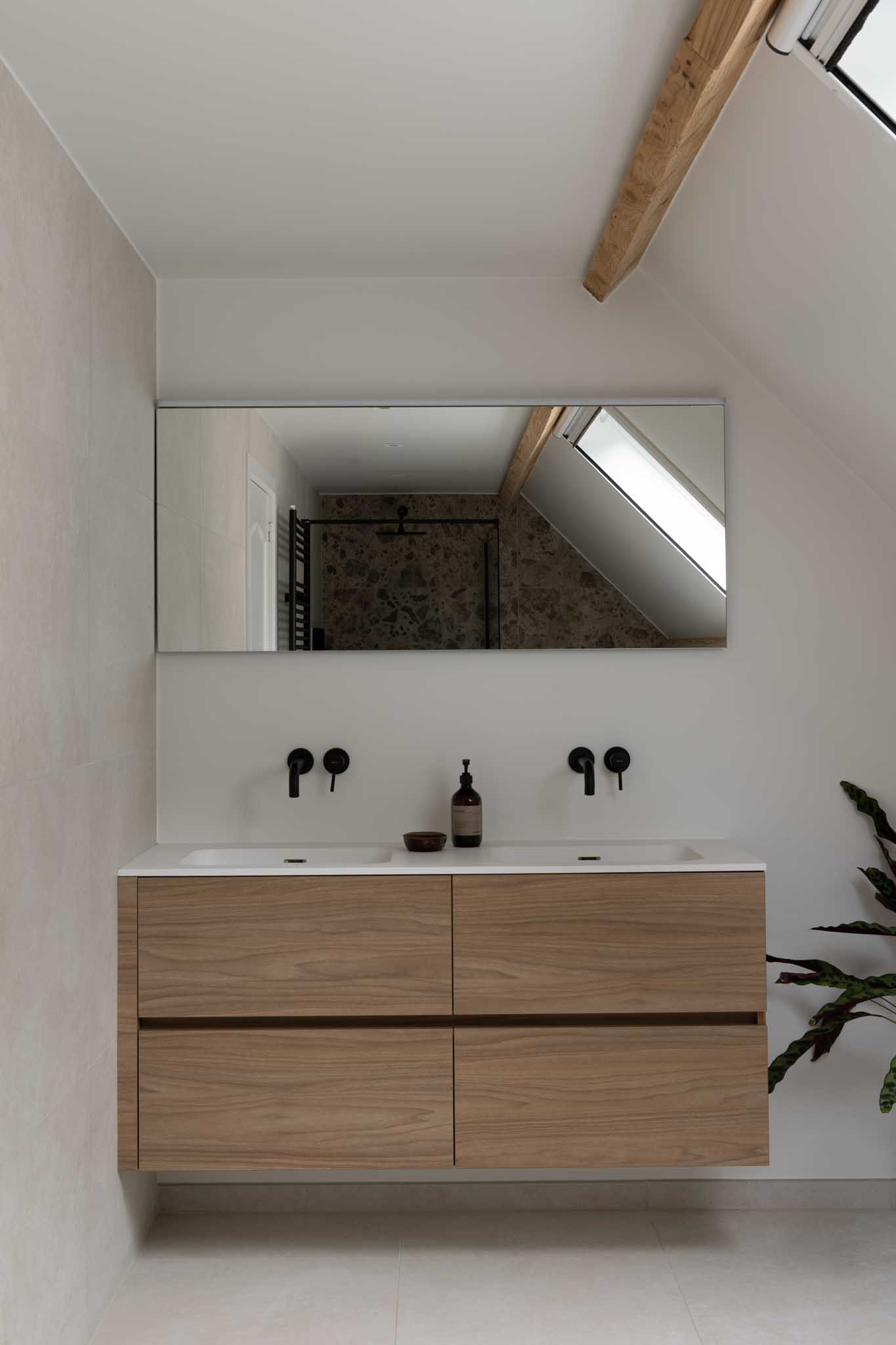 Moderne badkamerrenovatie met houten badkamermeubel, zwarte kranen en grote spiegel.