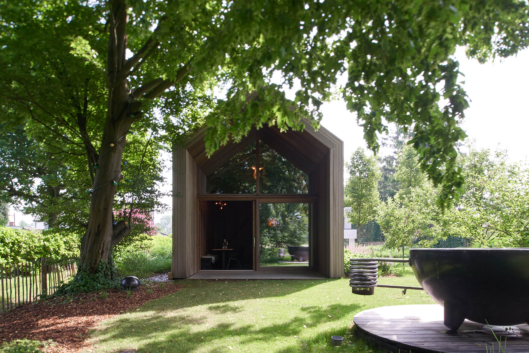 Voorgevel van houten tiny house met grote raampartij als duurzaam vakantiehuis midden in het groen, omgeven door bomen en natuur.
