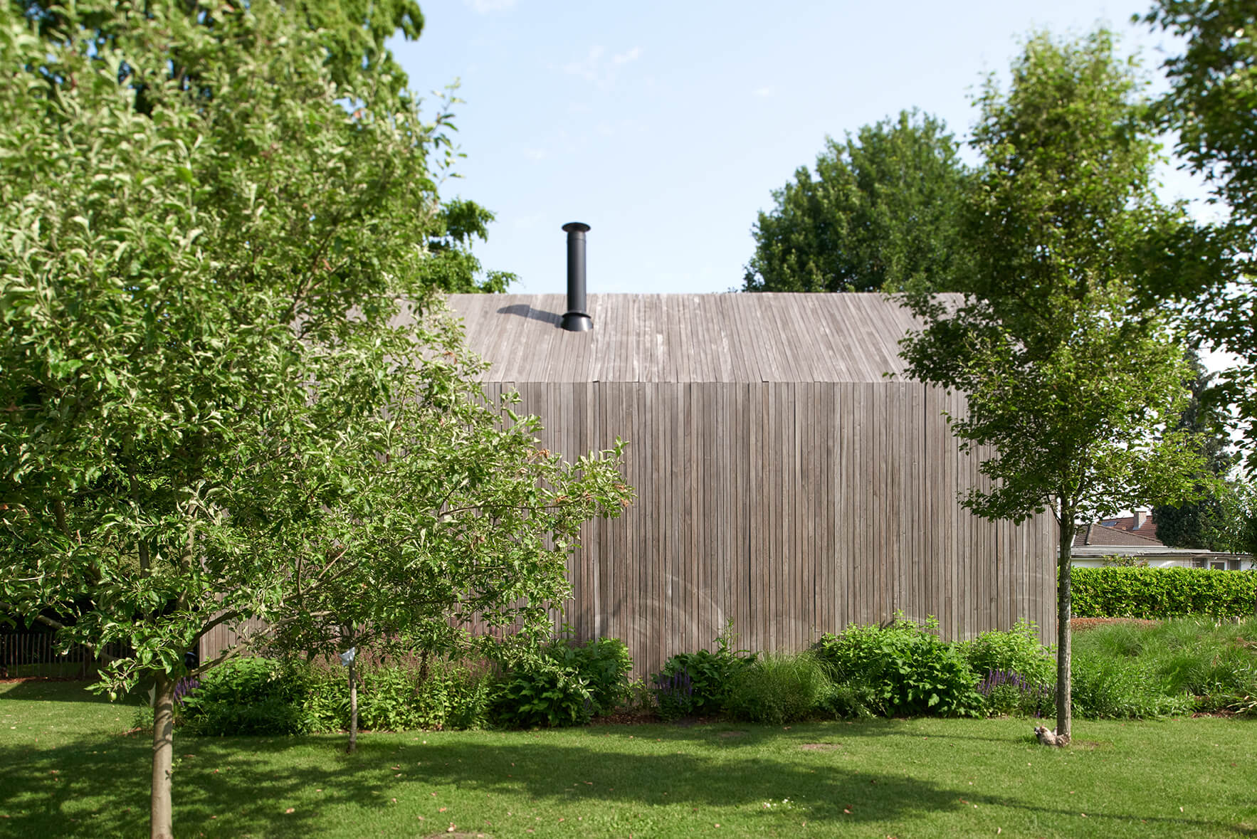 Zijgevel van tiny house uit houtskelet als duurzaam vakantiehuis midden in het groen, omgeven door bomen en natuur.