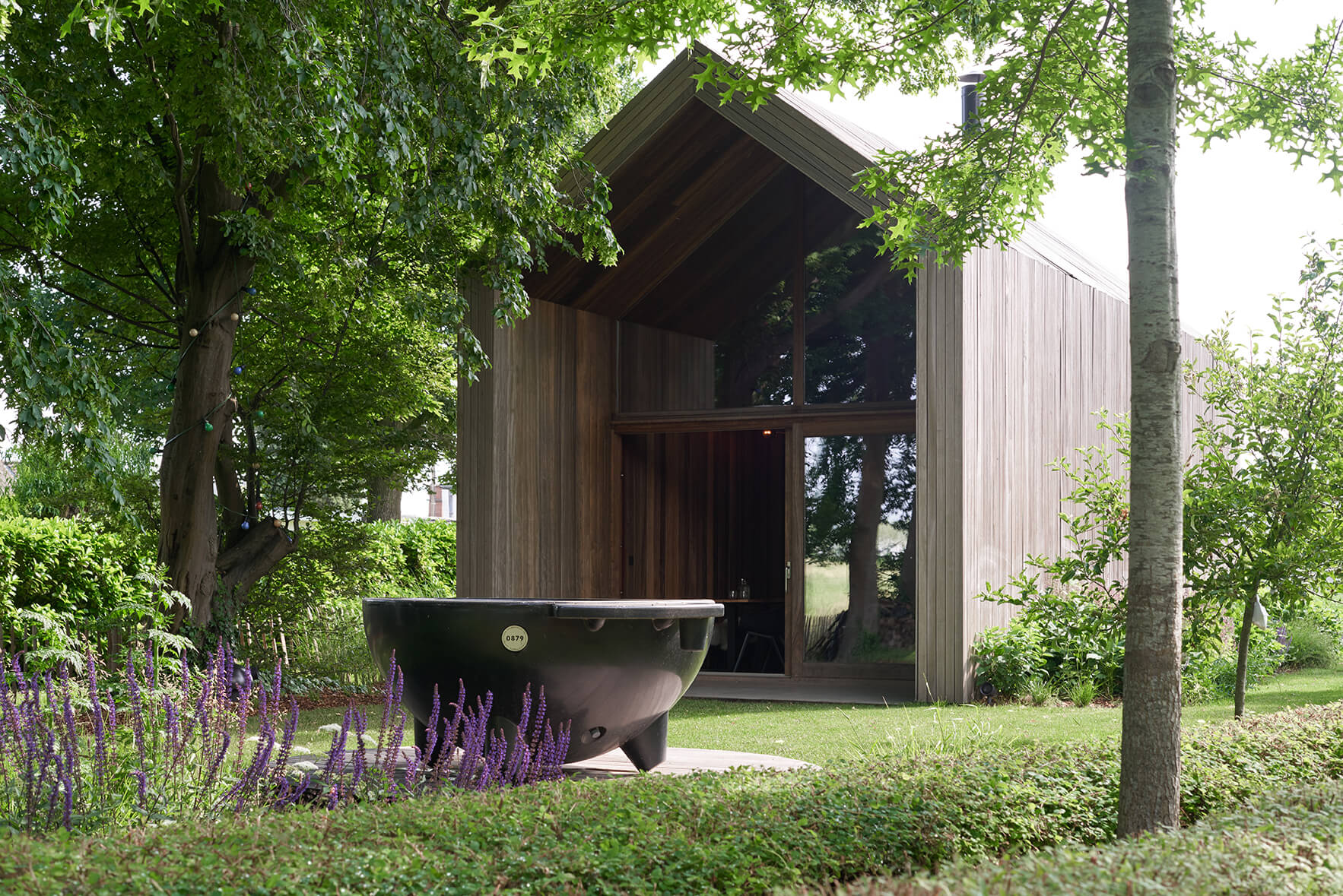 Houten tiny house met grote raampartij als duurzaam vakantiehuis midden in het groen, omgeven door bomen en natuur.