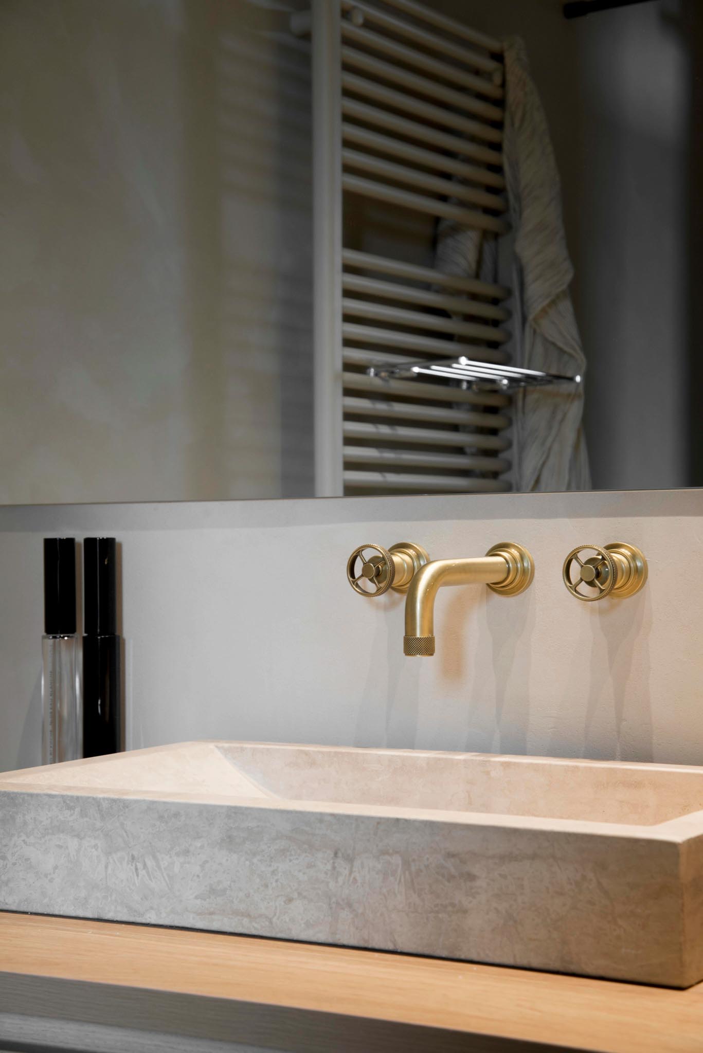 Moderne badkamerrenovatie met spoelbak uit natuursteen, gouden kranen en grote spiegel.