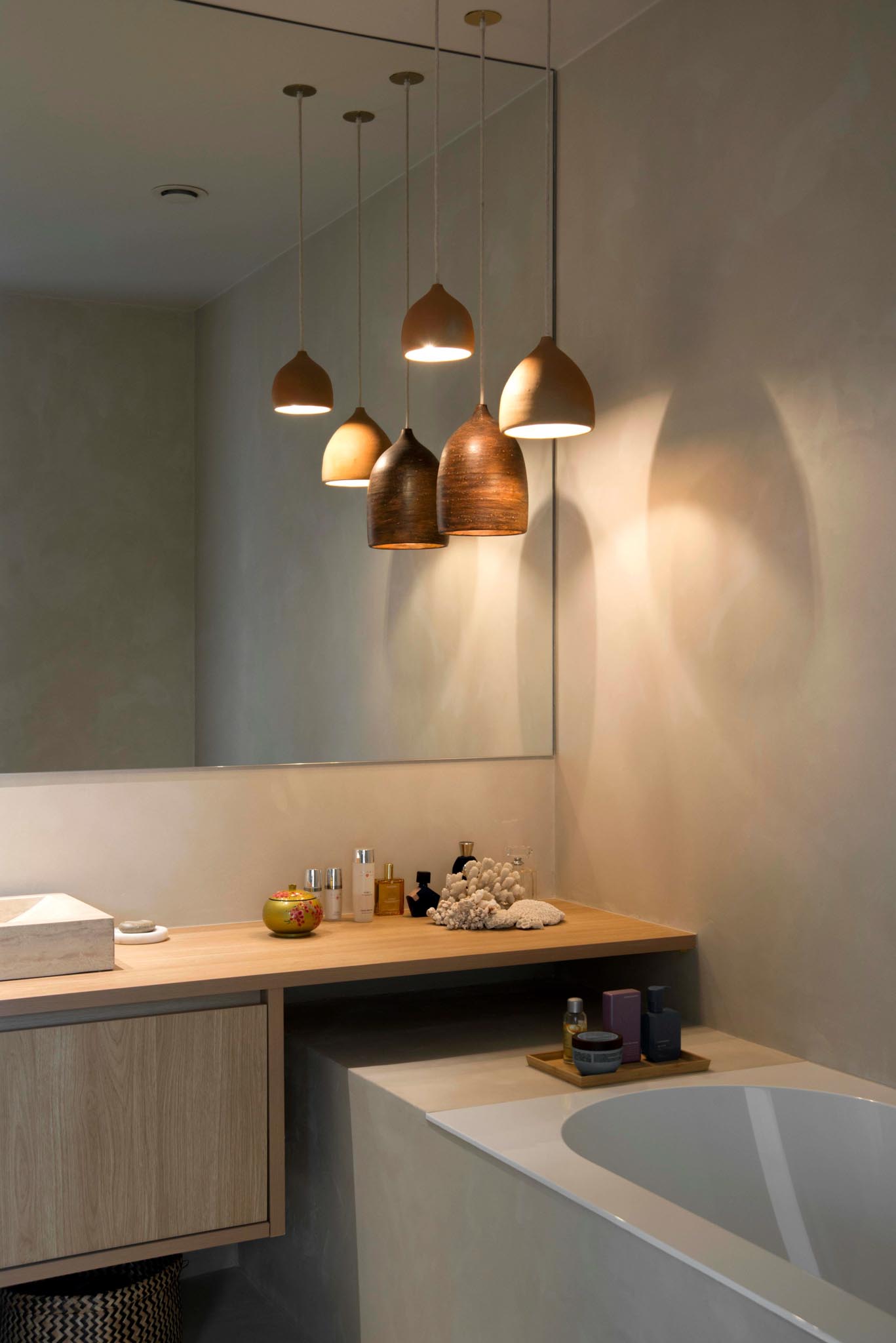 Moderne badkamerrenovatie met zachte kleuren, houten badkamermeubel, grote spiegel en hanglampen.