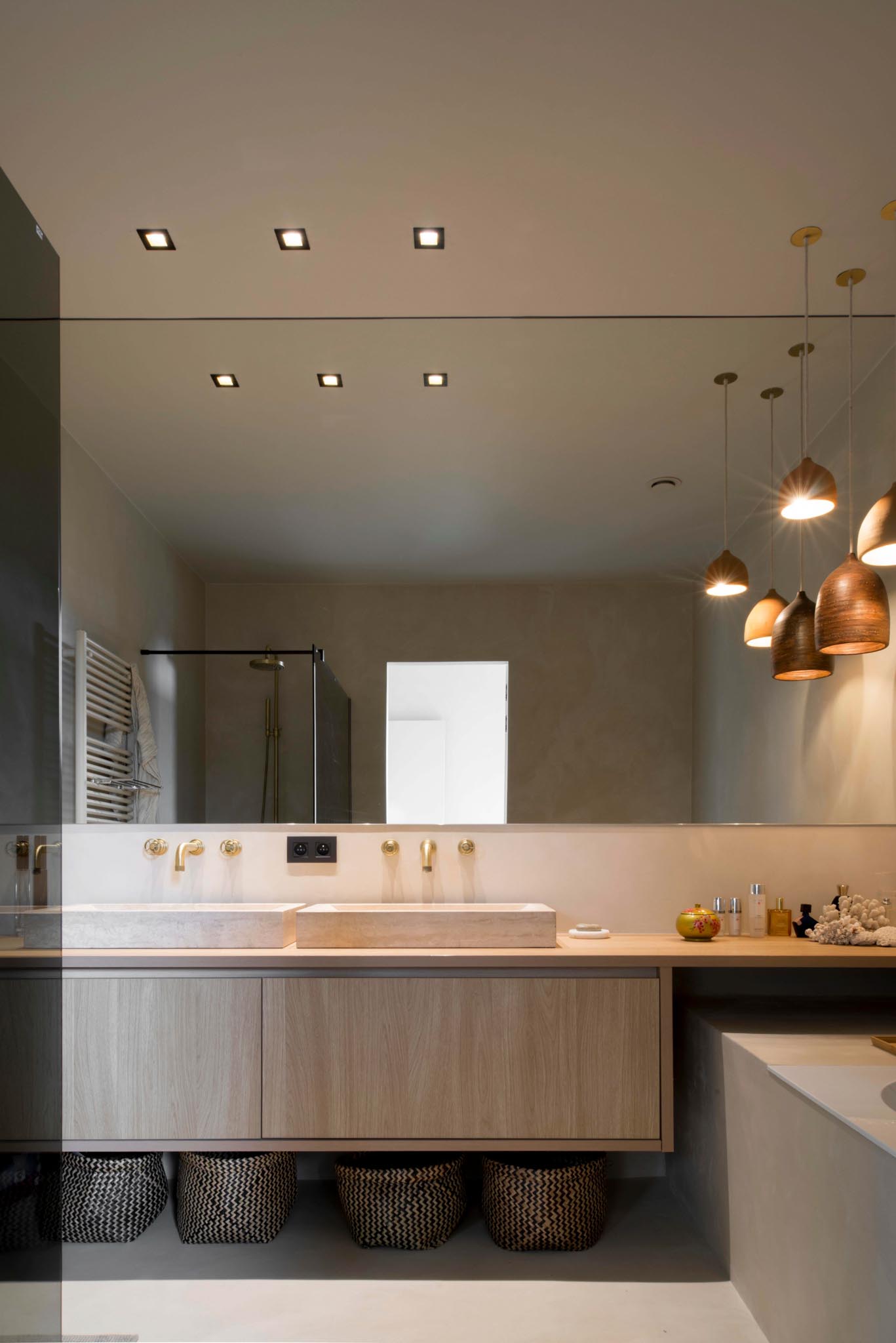 Moderne badkamerrenovatie met houten badkamermeubel, dubbele lavabo en grote spiegel tot tegen het plafond.