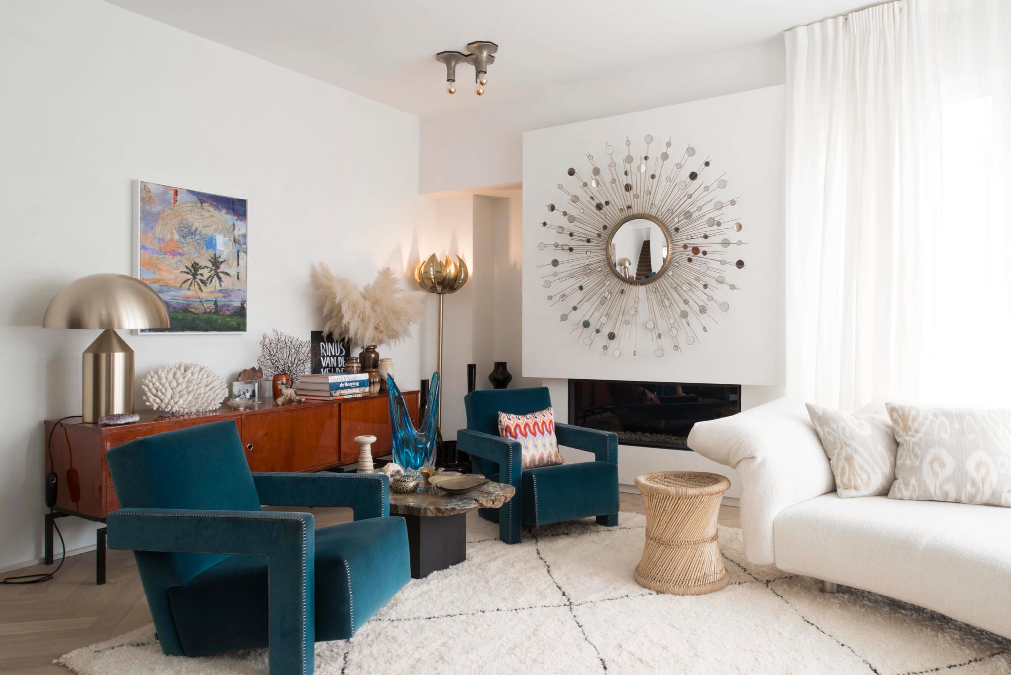 Leefruimte na totaalrenovatie met vloertapijt, blauwe en witte zetels, haardvuur en decoratie.