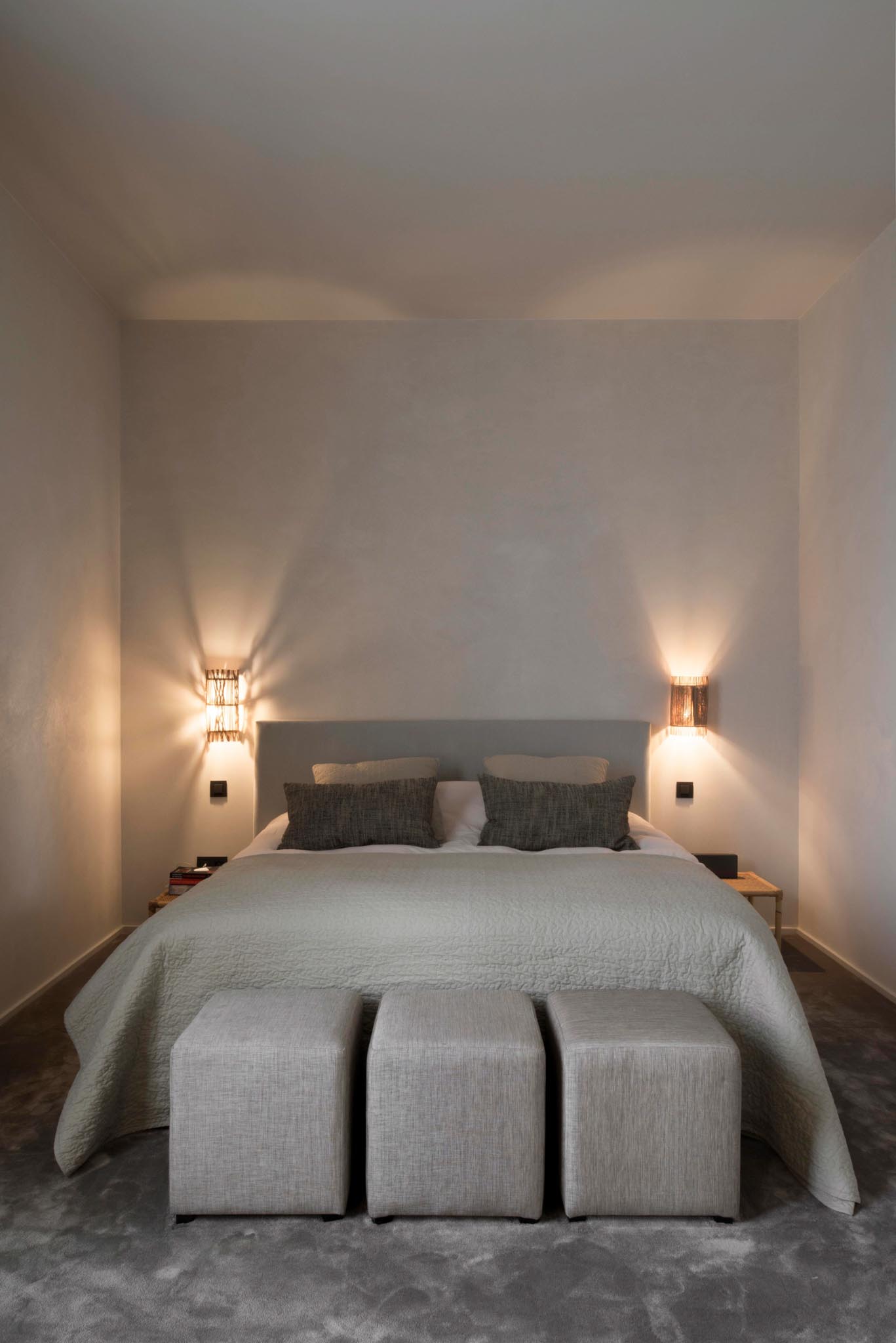 Rustige slaapkamer na totaalrenovatie met zachte kleuren, tweepersoonsbed en wandlampen.