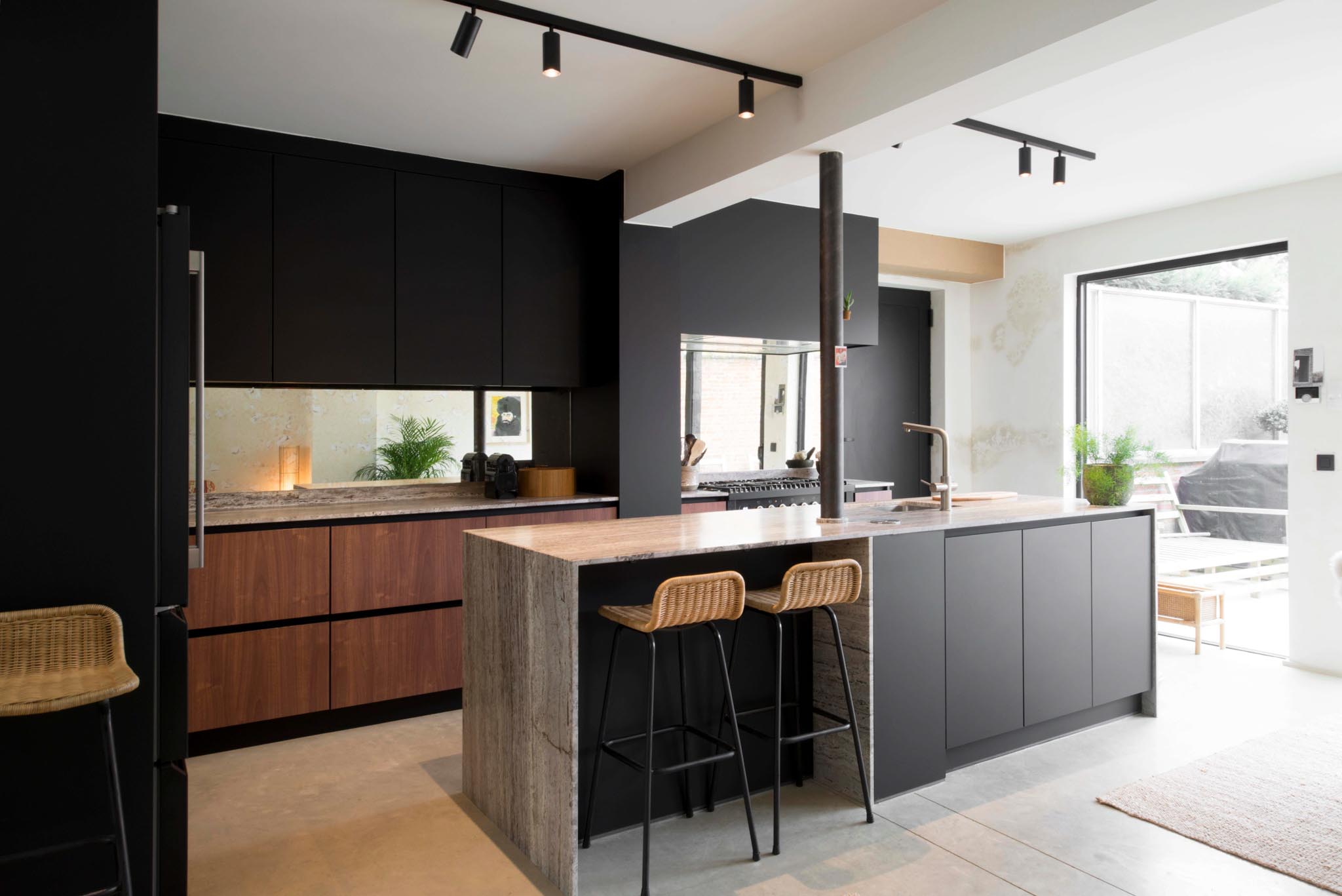 Keuken na totaalrenovatie met werkblad uit natuursteen, zwarte en houten kasten en groot raampartij naar de tuin.