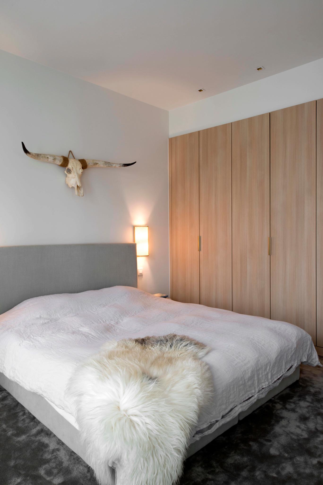 Slaapkamer na totaalrenovatie met tweepersoonsbed houten inbouwkasten en wanddecoratie.