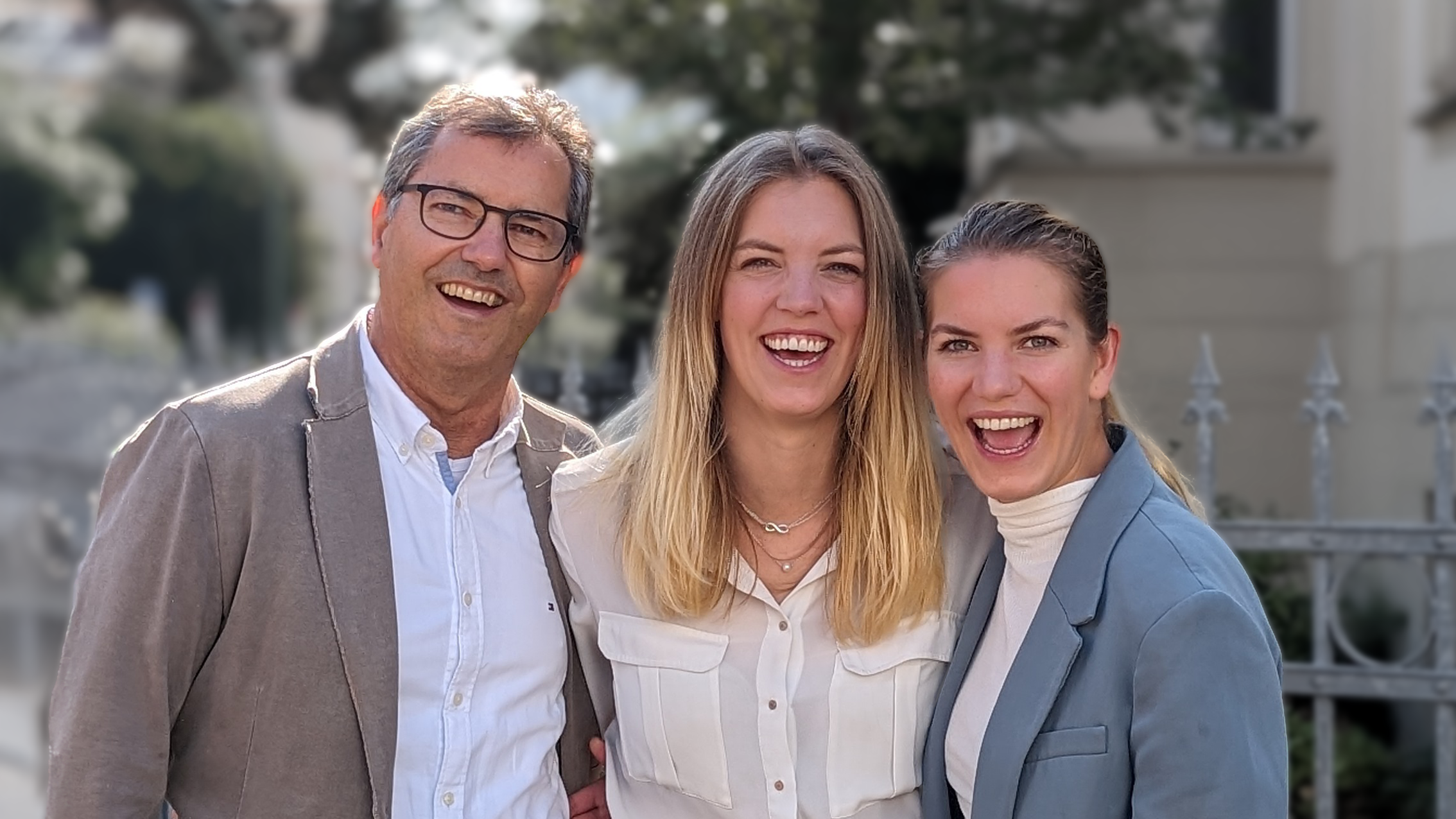 Drei fröhliche Personen, zwei Frauen und ein Mann, stehen eng zusammen und lachen.