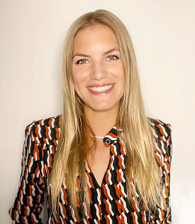 Lächelnde blonde Frau mit langem Haar, die ein schwarz-orange-weiß gemustertes Hemd trägt.