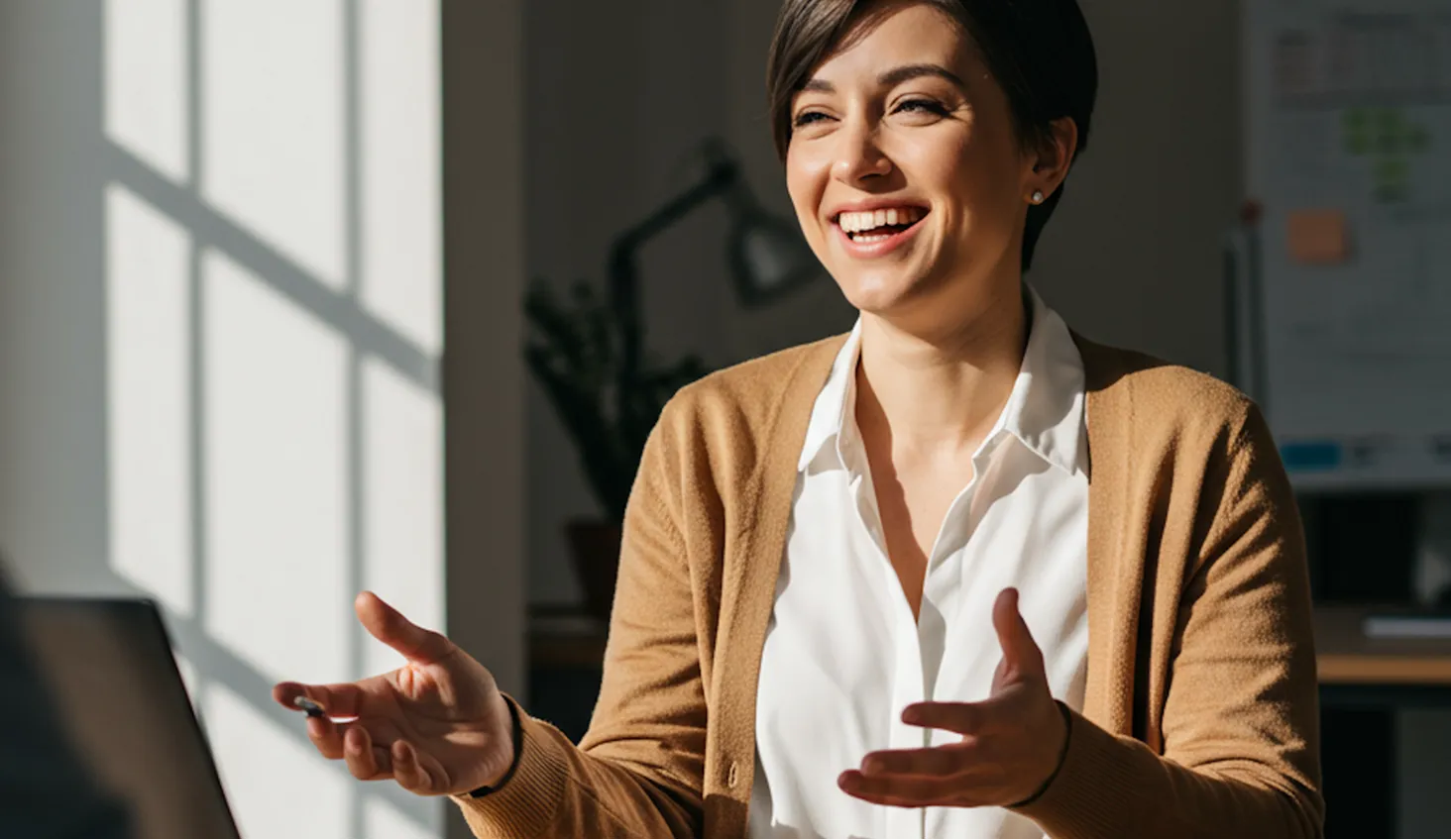 Smiling woman working on a laptop at a desk in natural light.