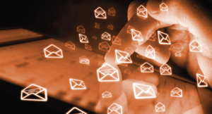 Hand tippt auf einer Tastatur mit schwebenden E-Mail-Symbolen darüber in orangefarbenem Licht.