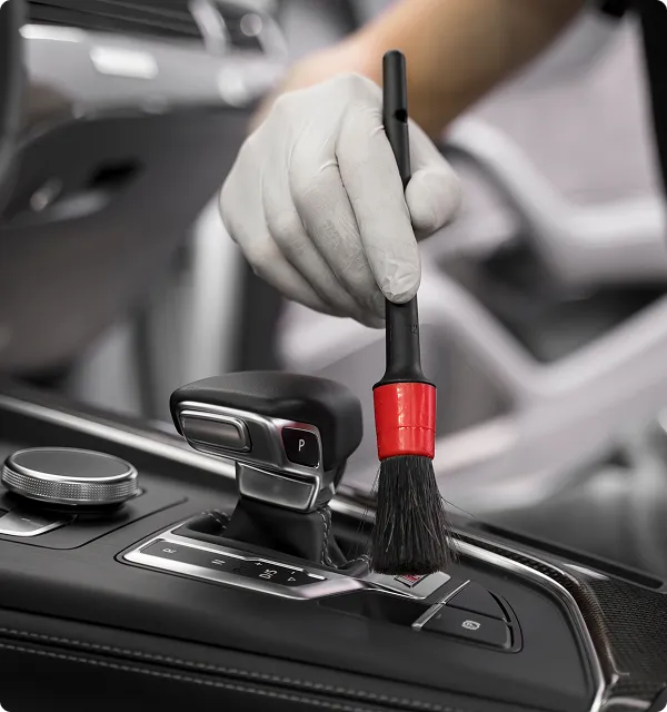 Hand wearing a white glove using a small brush to clean the gear shift panel inside a car.