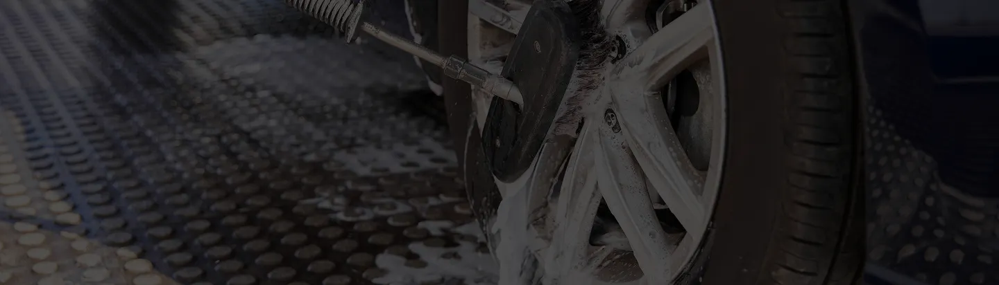 Close-up of a car wheel being cleaned with a rotating brush on a textured floor.