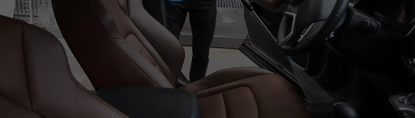 Interior view of a car showing brown leather seats and an open door with part of a person standing outside.