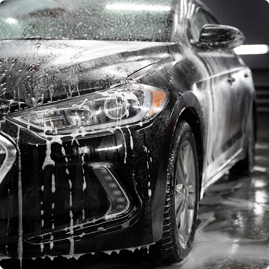 Close-up of a black car being washed with soap suds and water dripping down the front and side.