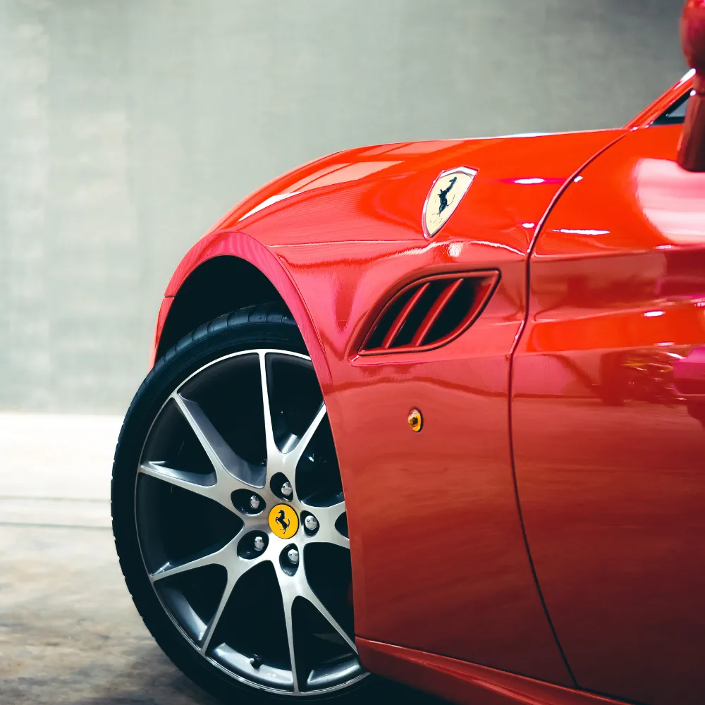 Close-up of the front wheel and side vent of a red Ferrari sports car.
