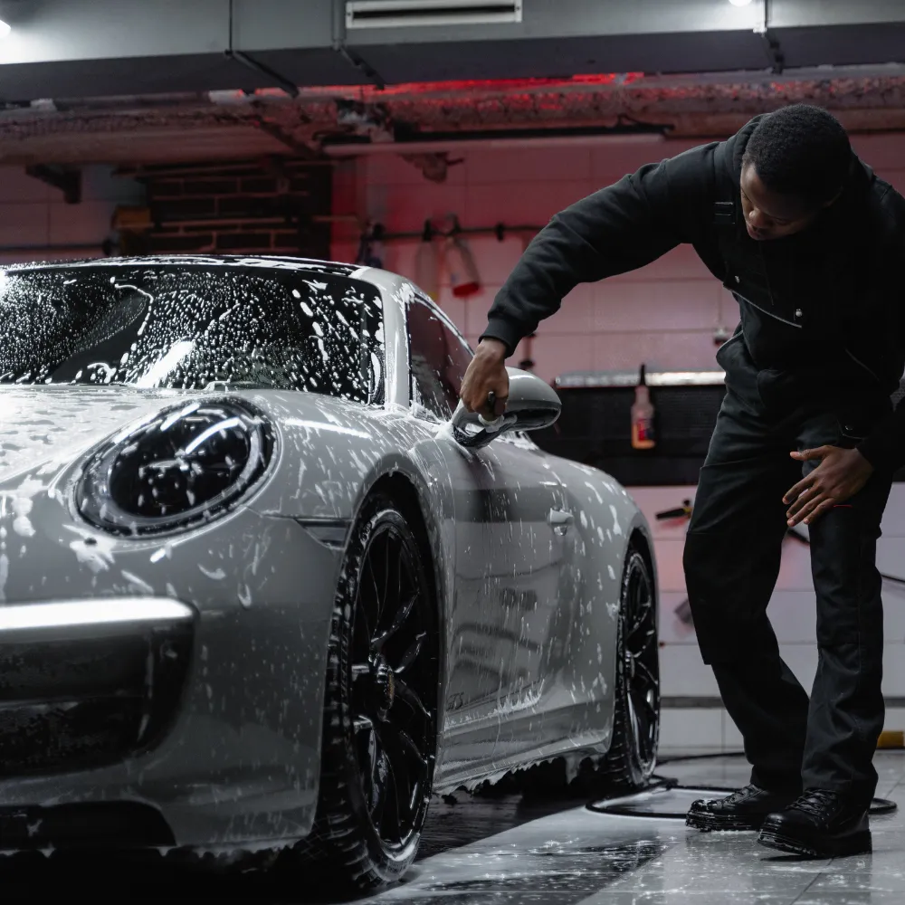 Person washing a white sports car covered in soap suds in an indoor garage.