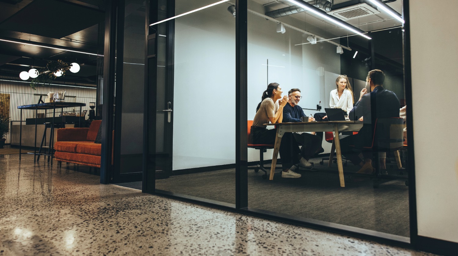 Four professionals having a meeting around a table inside a glass-walled office.