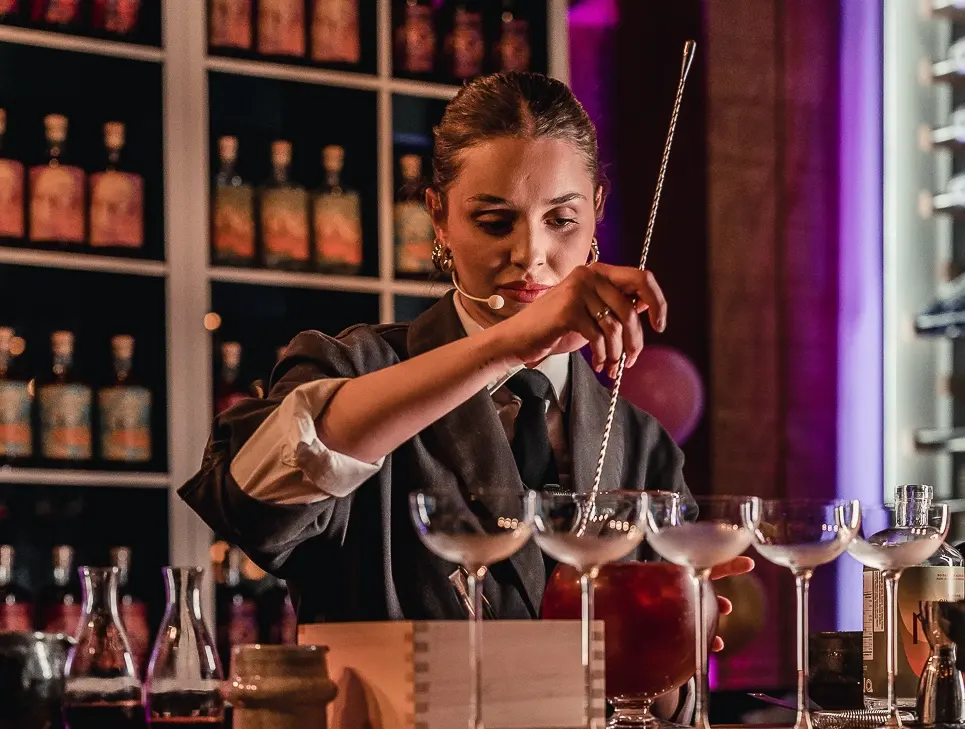 A woman bartender stirring her drink in a dim light bar