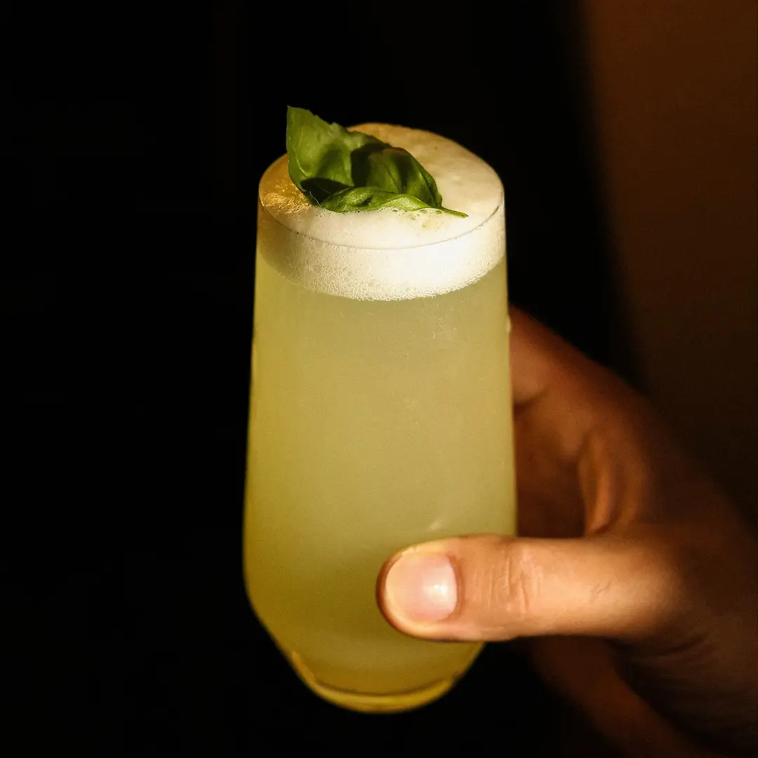 Non-alcoholic Garden fizz cocktail held by a man's hand on a dark background