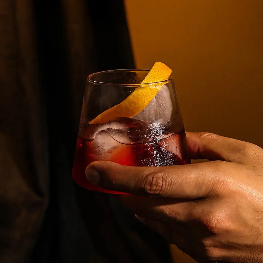 Non-alcoholic Espresso negroni cocktail held by a man's hand on a dark background