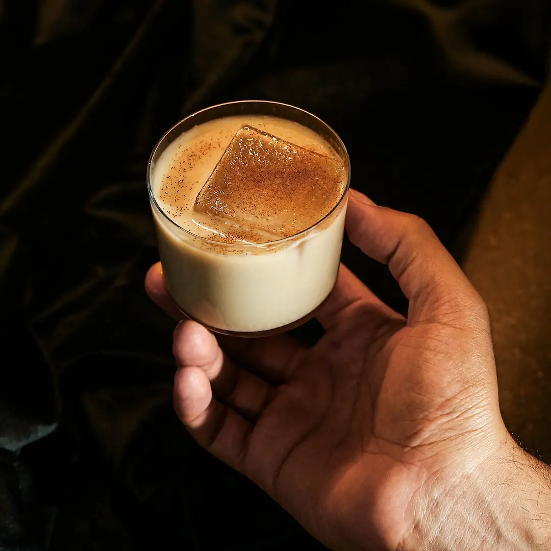 Non-alcoholic White russian cocktail held by a man's hand on a dark background