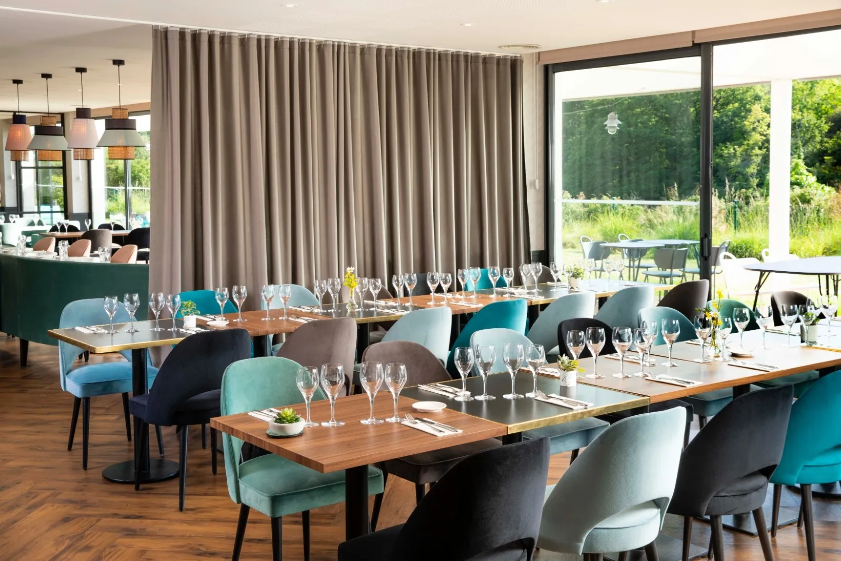 The bright Terrasse du Ter restaurant with set tables, colorful chairs, and large windows overlooking a green outdoor area.