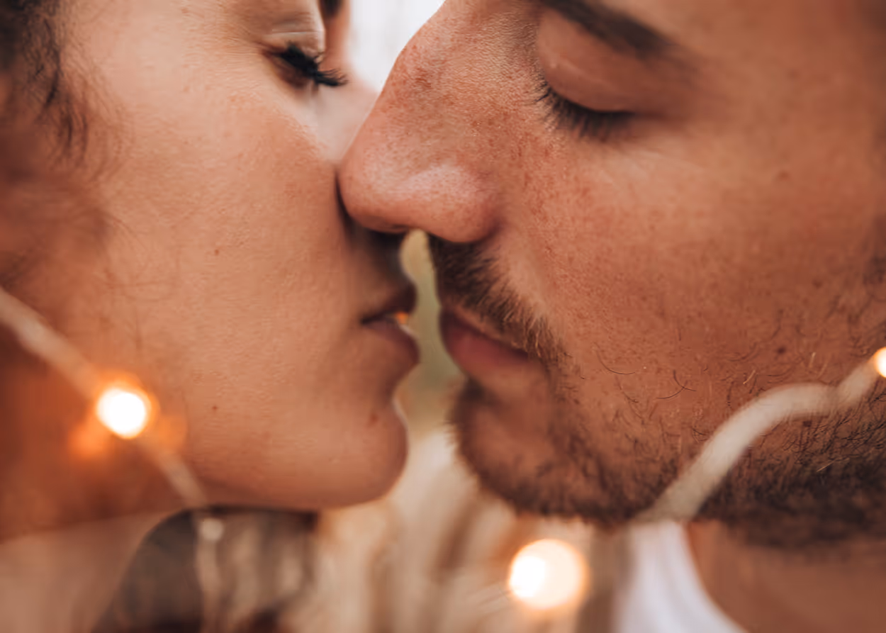 Close-up of a couple about to kiss with their eyes closed surrounded by soft glowing lights.