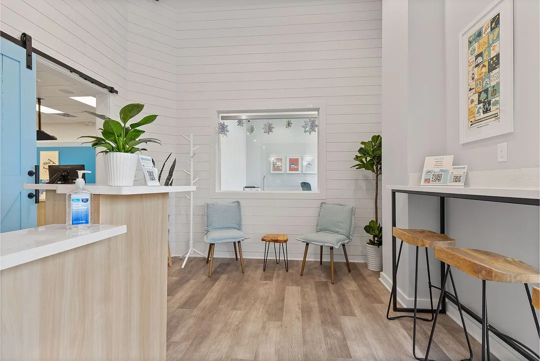 A room with a counter, chairs and a potted plant.