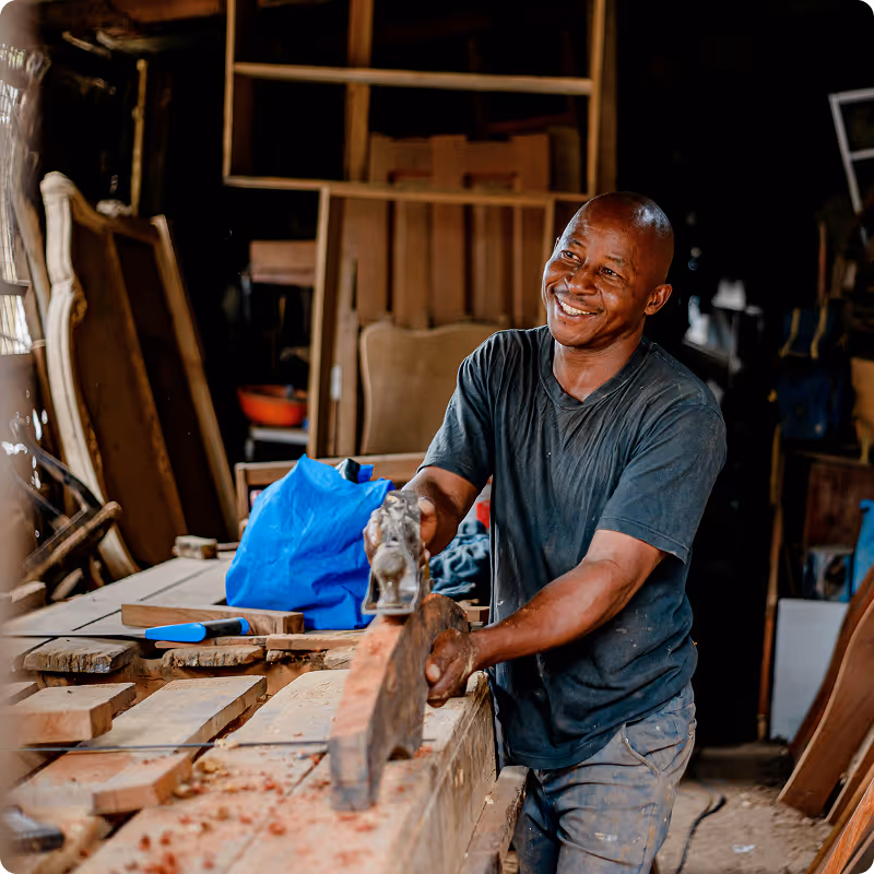 Smiling carpenter working with a hand planer on a wooden plank in a workshop.