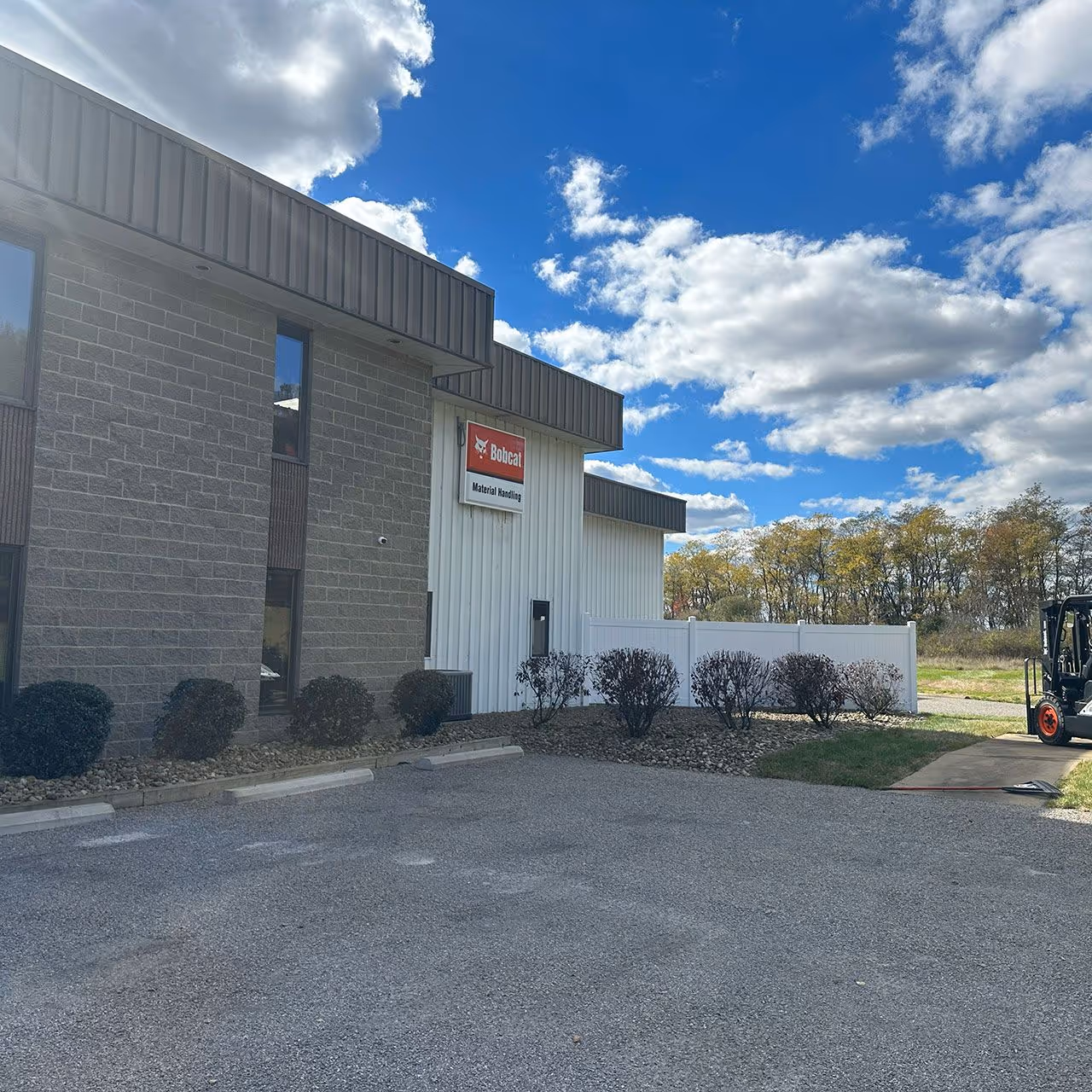 Industrial building with a Bobcat Material Handling sign under a blue sky with scattered clouds and a forklift parked on the side.