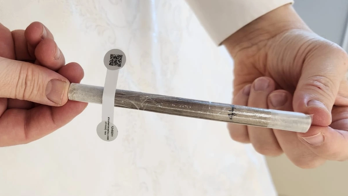 Hands holding a clear mezuzah case with a QR code sticker on its side