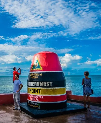 Southernmost Point buoy in Key West, Florida, with people taking photos against a blue sky and ocean backdrop.