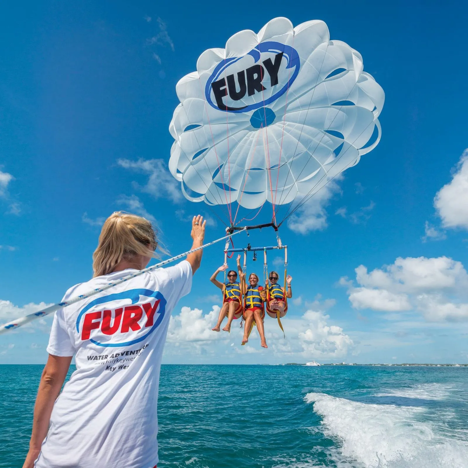 3 pretty ladies parasailing on a sunny day, surrounded by white clouds and blue sky.