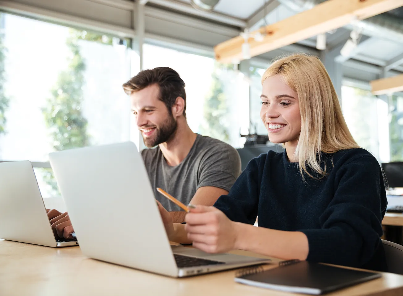 Smiling young man and woman working together on laptops in a bright office space.