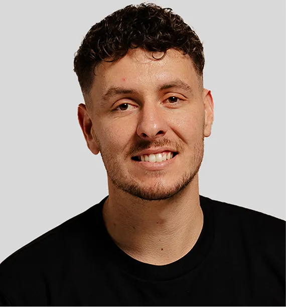 Smiling man with short curly hair and trimmed beard wearing a black shirt against a light gray background.