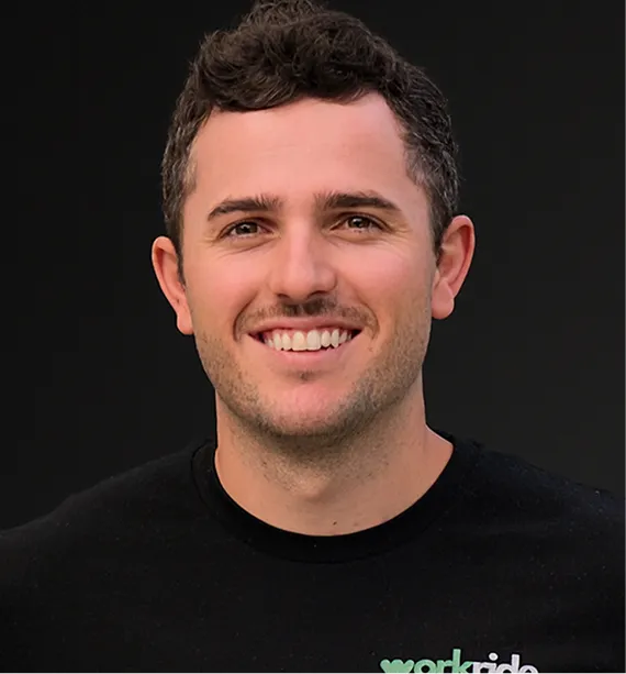 Smiling man with short curly hair wearing a black shirt with partial 'workr...' logo on a black background.