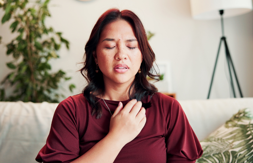 A person with eyes closed places a hand on their chest, appearing to be experiencing discomfort or pain.