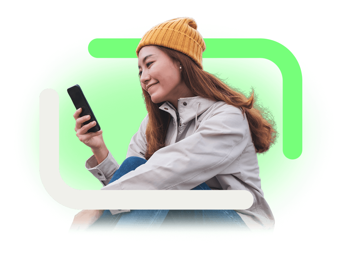 A woman sits smiling looking at her mobile device.