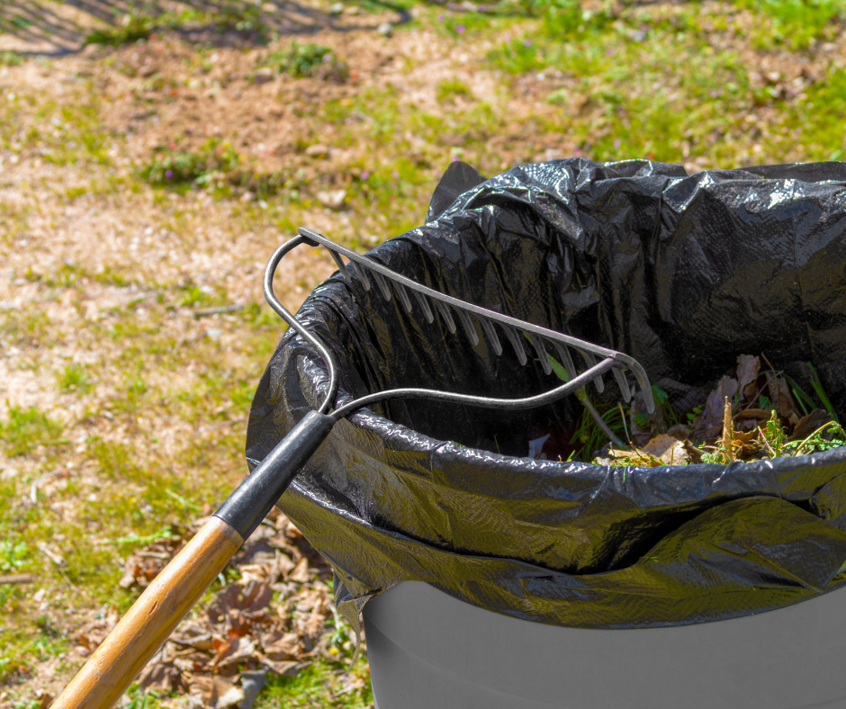 A metal rake leaning against a trash bin filled with lawn clippings.