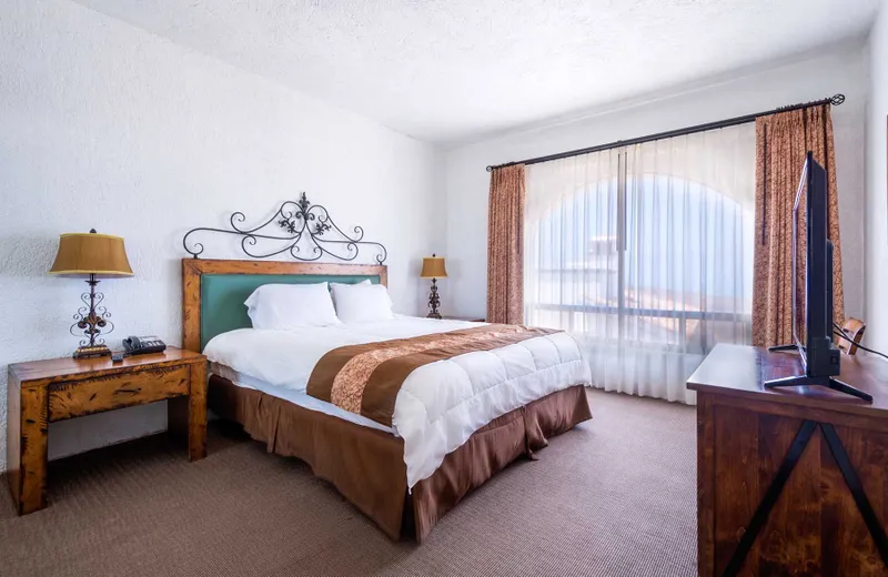 Habitación de hotel con cama grande, dos lámparas, TV y ventana con vista al mar.