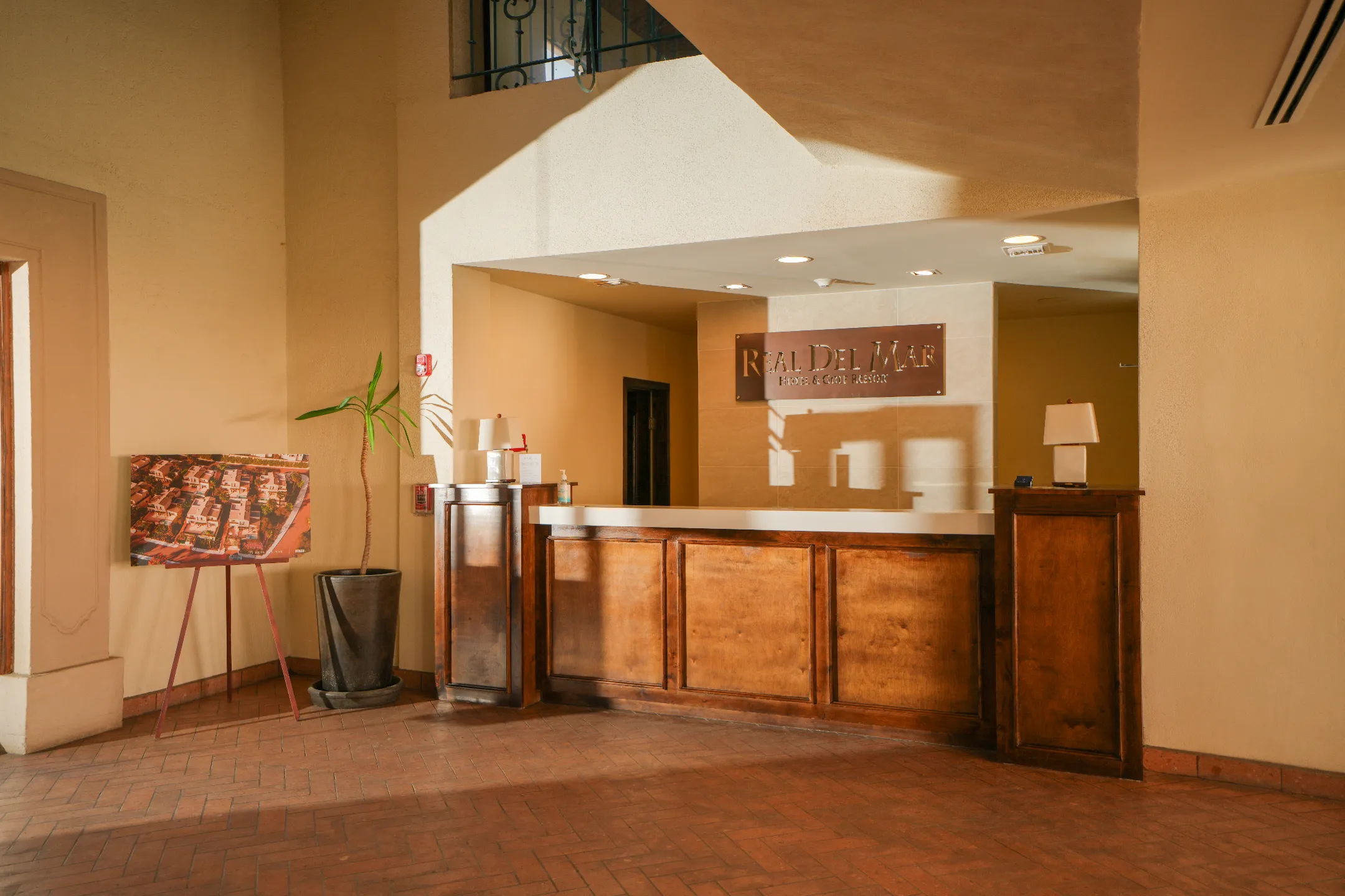 Recepción del hotel con mostrador de madera, lámparas y planta junto a un cartel con plano.