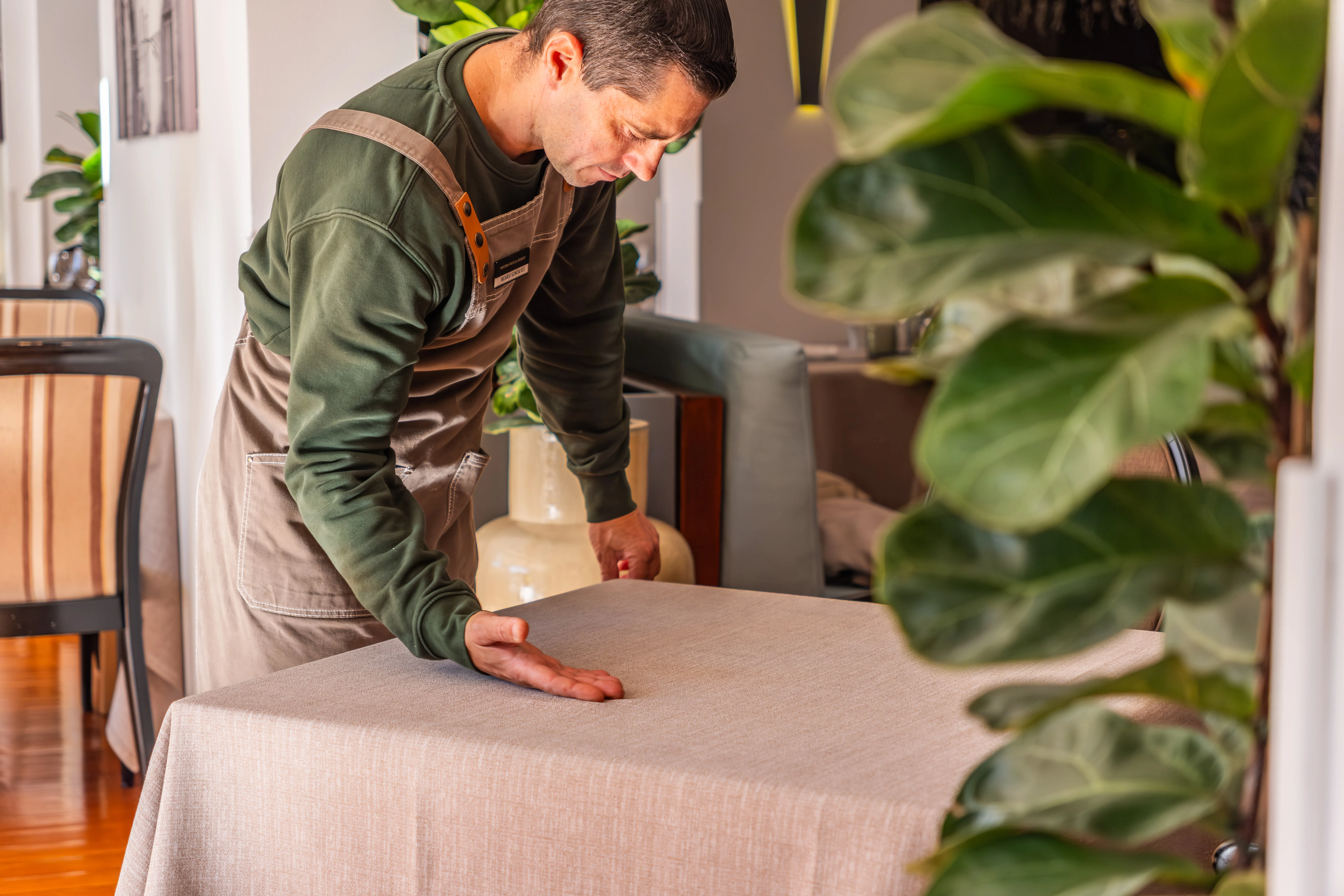 Colaborador a preparar mesa com têxteis limpos e bem apresentados em espaço de restauração.
